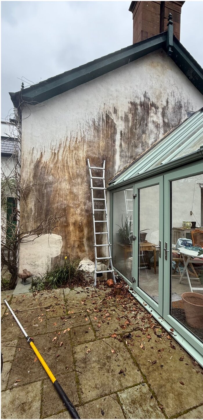 Rendered gable wall streaked brown with organic growth before soft washing